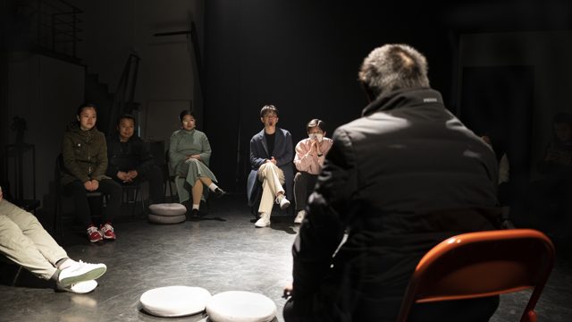 坐姿人物背对镜头，其他人围坐面对其方向