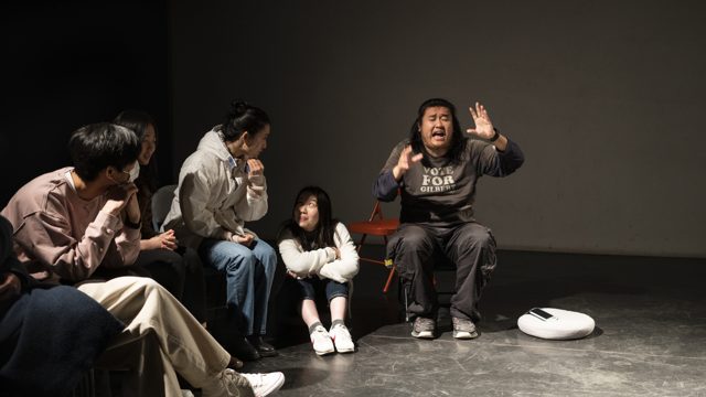 一人坐姿张口并举起双手，旁人转头面向其方向