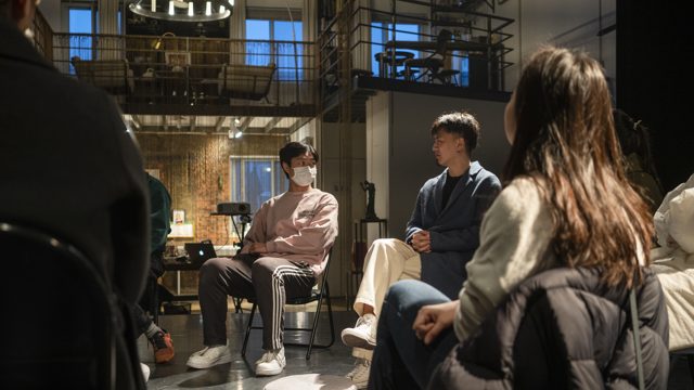 多人坐椅围坐，其中一人侧向说话姿态