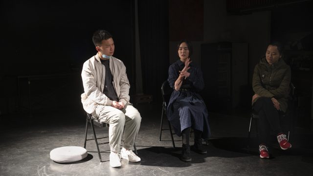 三人坐姿，中间一人双手在胸前展开