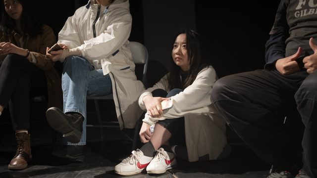 一人站立俯身伸手，旁人坐着