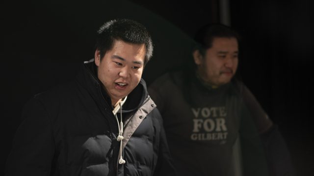 坐姿人物前倾，旁人位于后方