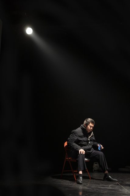 远景中一人坐在橙色椅子上，顶部灯光照明